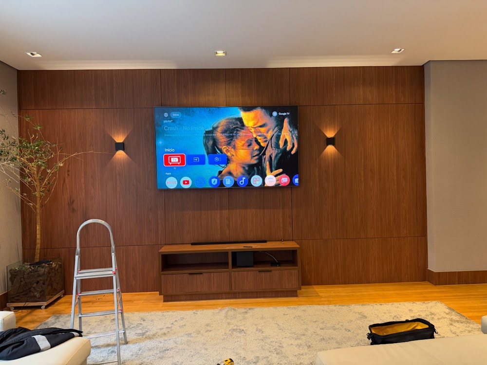 Sala com televisão e sistema de áudio instalados em painel de madeira